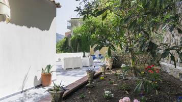 Een binnenplaats met plantenpotten, een witte muur en tuinmeubilair.
