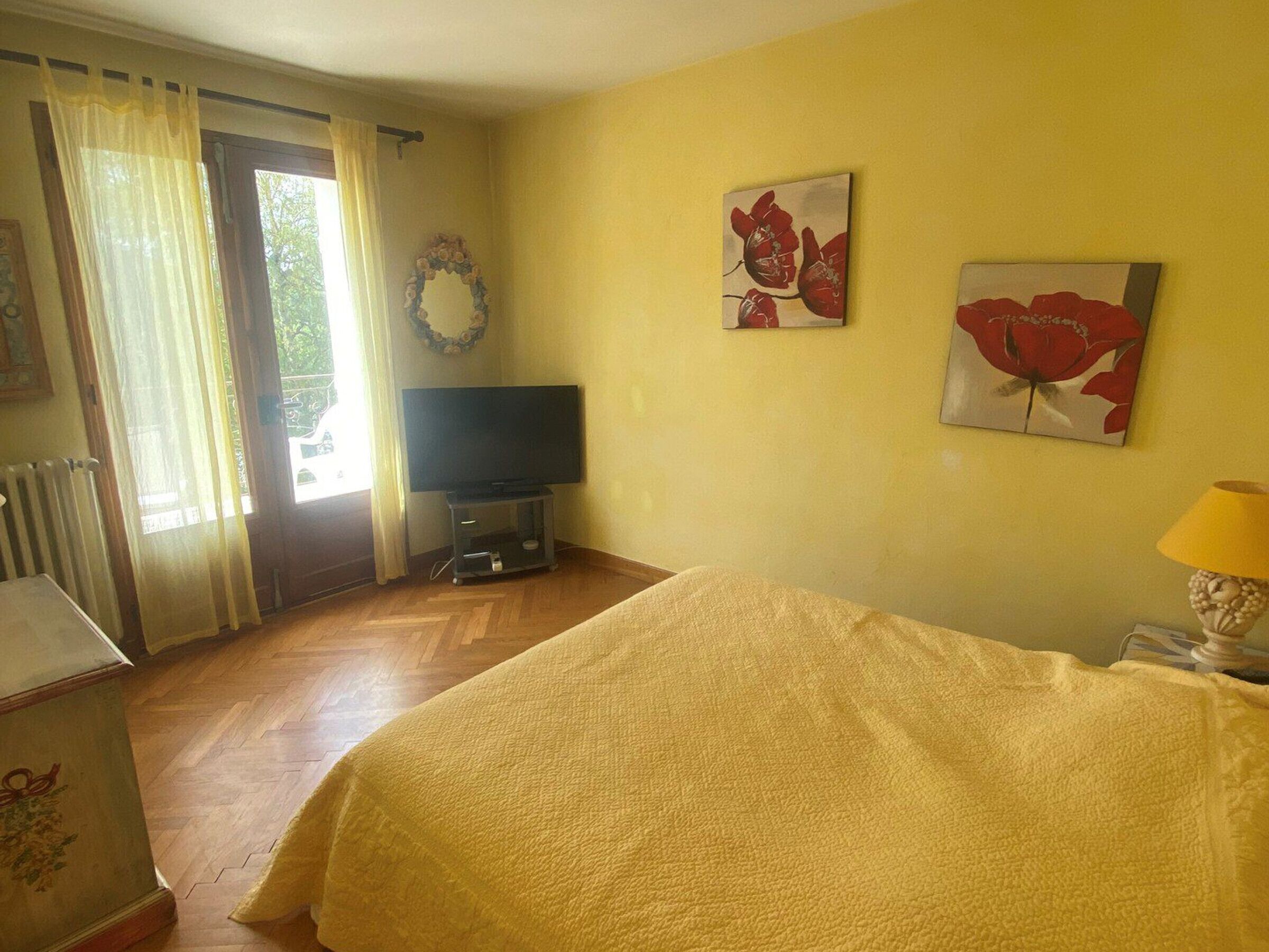 A bedroom with a bed, a television on a stand, and two paintings on the wall.