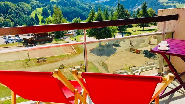 A balcony with red chairs and a table, overlooking a parking area and a green landscape with trees and hills. - 3-room apartment at the foot of the slopes in Villard-de-Lans (Villard-de-Lans)