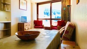 A cozy living room with a wooden table, a red sofa, and a television on a wooden cabinet. - 3-room apartment at the foot of the slopes in Villard-de-Lans (Villard-de-Lans)
