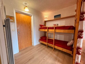 A room with a bunk bed, a door, a radiator, and a wall-mounted light fixture.