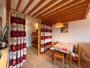 A cozy room with a wooden ceiling, a table with a patterned tablecloth, and a bunk bed with red and white curtains.