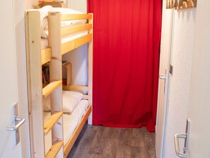 A bunk bed room with a red curtain, a wooden door, and a white wall.