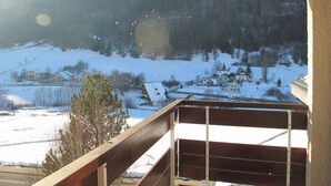 A view from a balcony overlooking a snowy landscape with houses and a forested hill in the background. - Studio cabin with balcony, mountain view near village center (Villard-de-Lans)