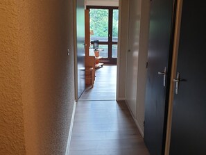 Un couloir au plancher de bois mène à une pièce dotée d’une grande fenêtre.