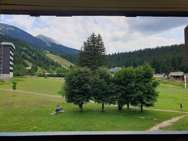 A view of a grassy area with trees, a building, and mountains in the background.