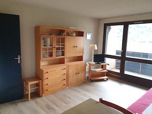 A room with a wooden cabinet, a desk, a chair, a lamp, and a sliding glass door to the outside.