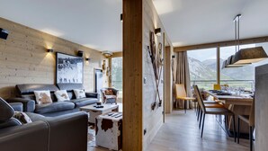 Un intérieur moderne avec un canapé, une table basse et un coin repas, des murs en bois et une vue sur les montagnes.
