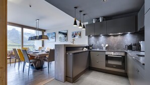 Une cuisine moderne avec des meubles de couleur sombre, un four encastré et des luminaires suspendus.