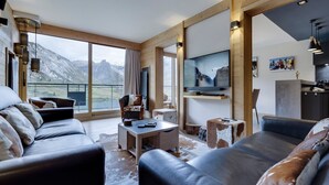 Un salon moderne avec des canapés en cuir, un téléviseur fixé au mur et une grande fenêtre donnant sur une vue imprenable sur les montagnes.