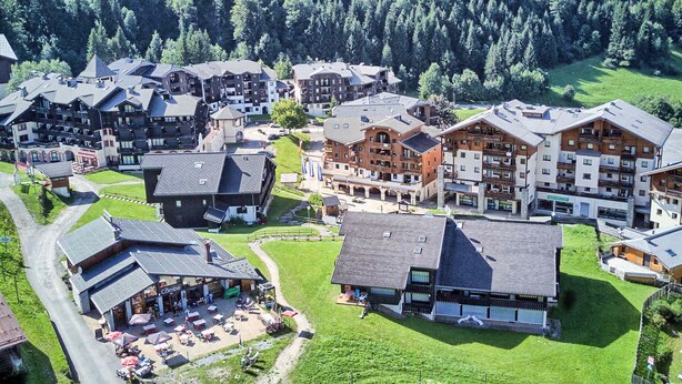 A mountainous village with multi-story buildings, a central square with outdoor seating, and a mountain backdrop. - 3-room apartment in Morillon 1100, 6 people, pets allowed, wifi (Morillon 1100)