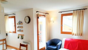 A cozy living room with a wooden table, a blue chair, a white sofa, a clock, and a window with curtains. - 3-room apartment in Morillon 1100, 6 people, pets allowed, wifi (Morillon 1100)