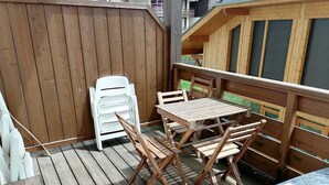 A wooden deck with a table and chairs, a white plastic chair, and a small table with a black top. - 3-room apartment in Morillon 1100, 6 people, pets allowed, wifi (Morillon 1100)