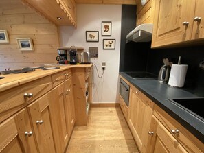 A narrow kitchen with wooden cabinets, a coffee maker, a kettle, and a toaster on the counter.