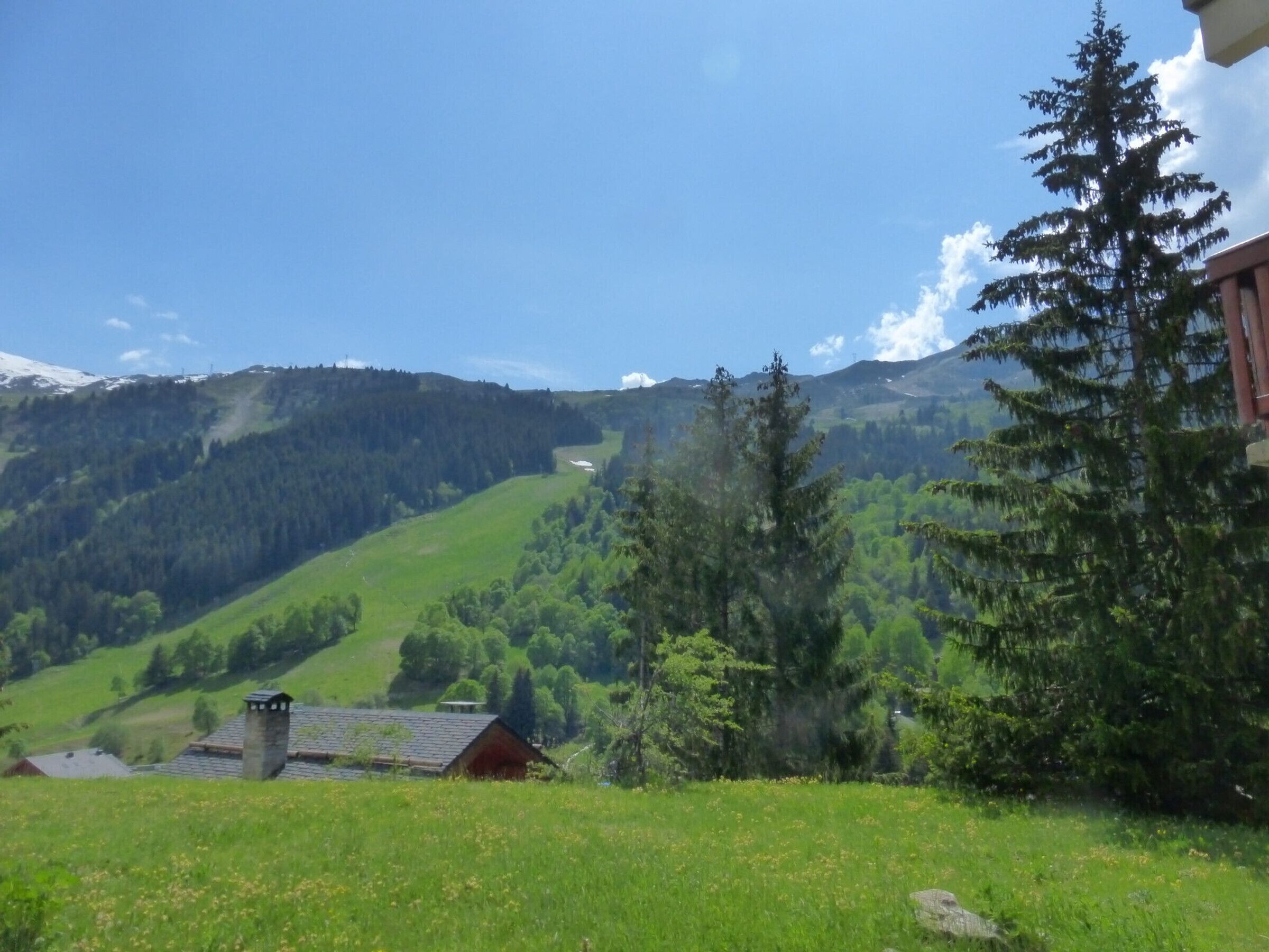 A rural landscape with a house on a hill, surrounded by greenery and mountains.