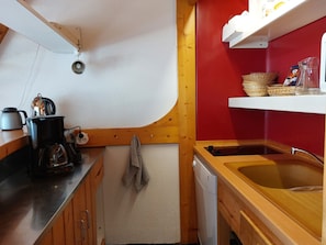 A compact kitchen with a wooden countertop, a coffee maker, a kettle, a dish rack, and a sink.