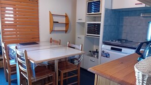 Een kleine keuken met een houten tafel en stoelen, een inbouwoven, een magnetron en een fornuis.