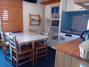 Een kleine keuken met een houten tafel en stoelen, een inbouwoven, een magnetron en een fornuis.