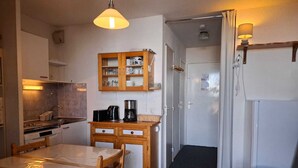 Een compacte keuken met een eettafel en stoelen, een koffiezetapparaat en een kast met servies.