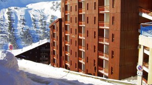 Een meerlaags gebouw met balkons, omgeven door met sneeuw bedekte bergen.