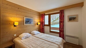 Ett rum med träpanel på väggarna, två sängar med vita sängkläder, ett fönster med röda gardiner och två vägglampor.