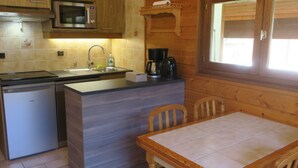 A compact kitchen with a built-in microwave, a sink, and a coffee maker. There is a small refrigerator and a wooden table with chairs. - 6-person apartment with south-facing balcony and parking in Châtel (Châtel)