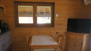 A wooden cabin interior with a dining table and chairs, a window with blinds, a television on a cabinet, and a kettle on the counter. - 6-person apartment with south-facing balcony and parking in Châtel (Châtel)