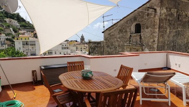 Eine Dachterrasse mit einem runden Holztisch und Stühlen, einem weißen Sonnensegel und Blick auf ein historisches Gebäude im Hintergrund.