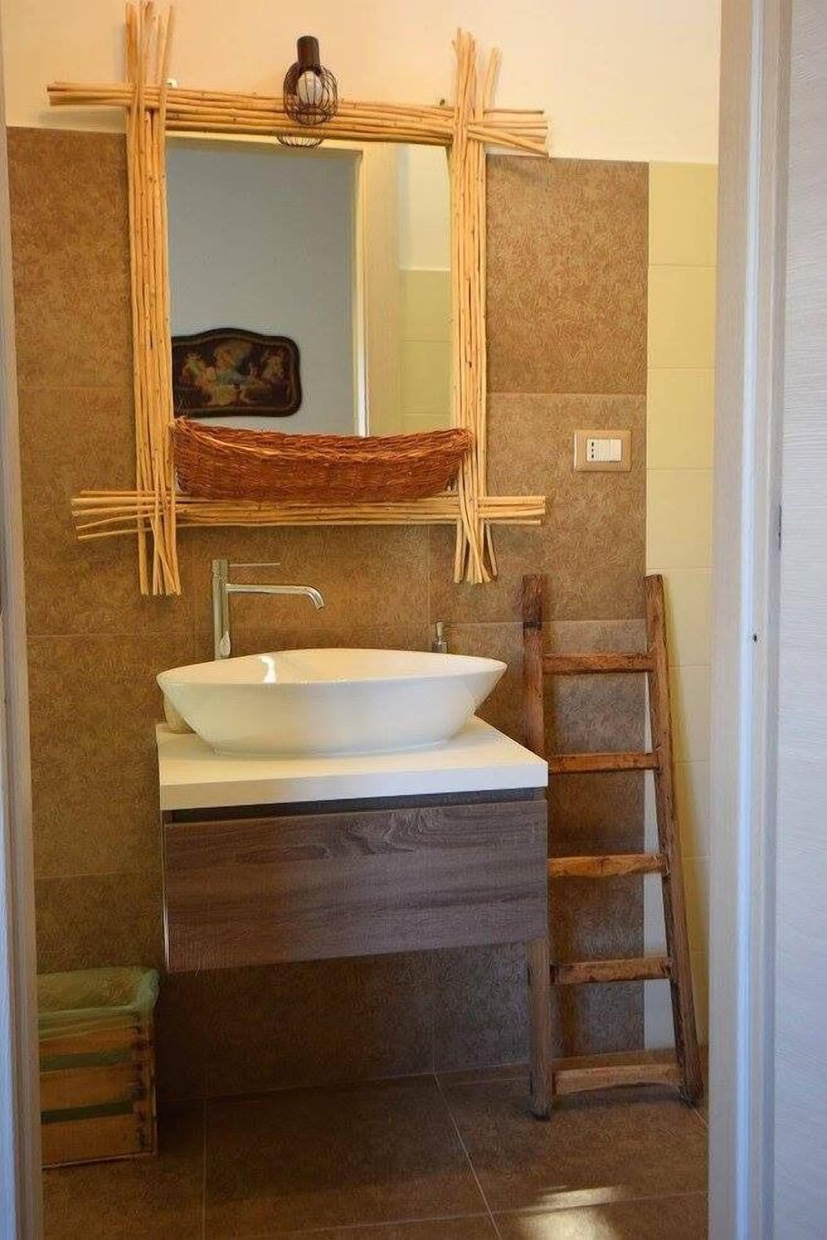 Ein Badezimmer mit einem weißen Waschtisch, einer Holzleiter und einem Spiegel mit gewebtem Rahmen.