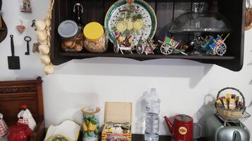 Un estante de cocina con varios objetos, incluyendo un plato con diseño de frutas, un frasco, una botella y una tetera.