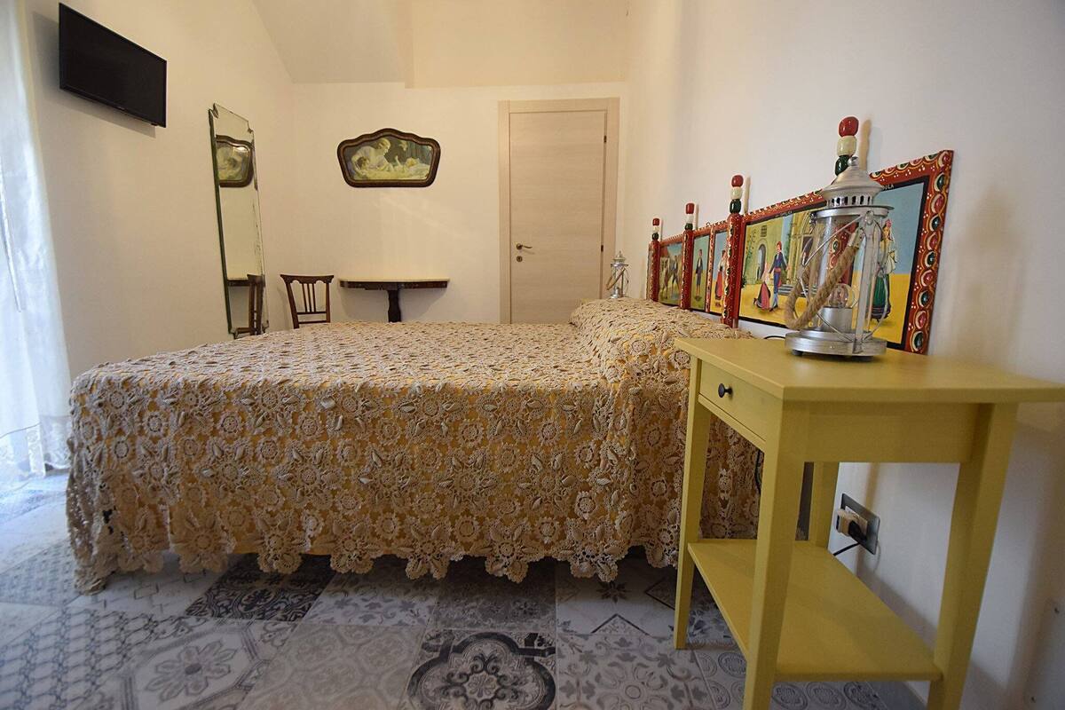 Un dormitorio con una cama, una mesita de noche, un espejo, una puerta y una pared con un cuadro enmarcado.