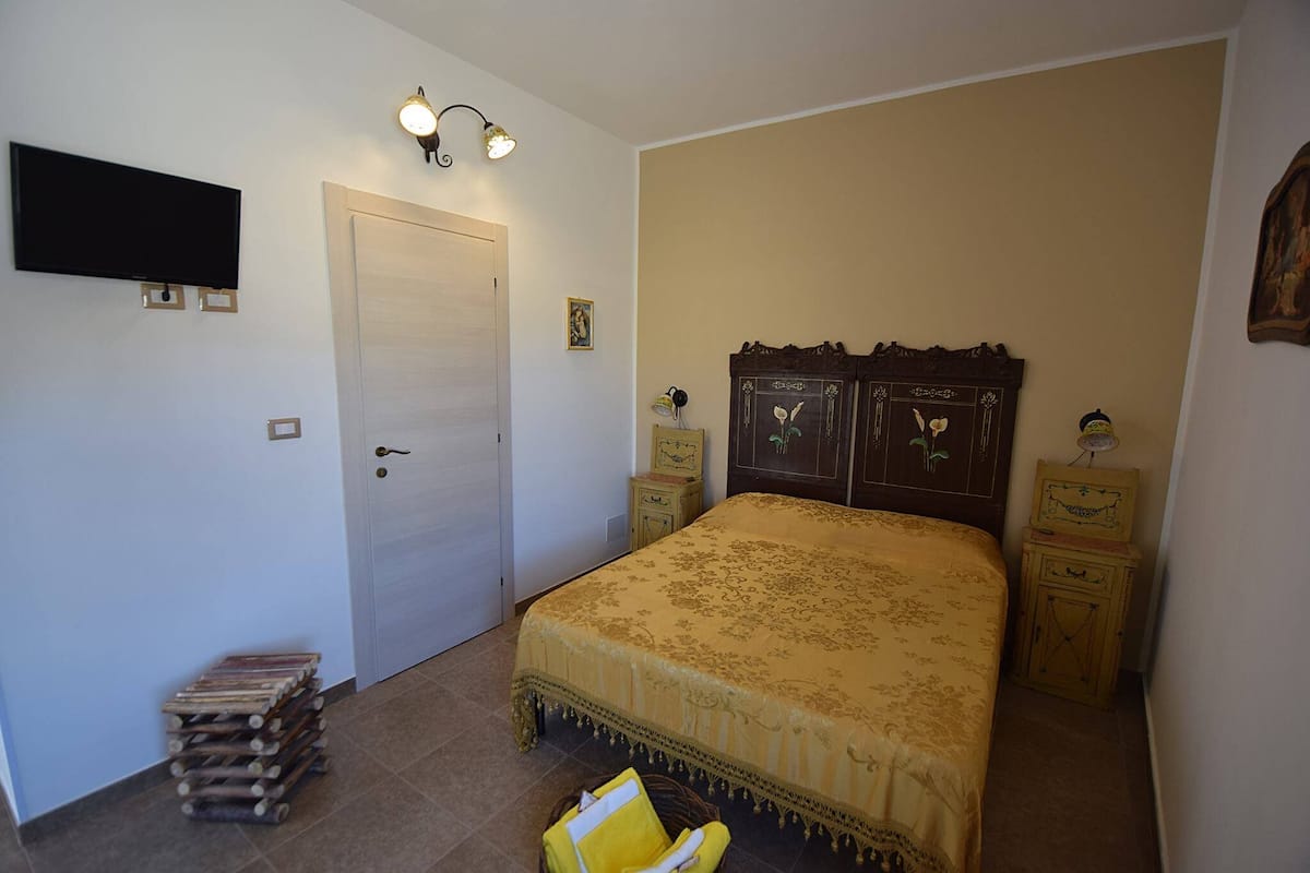 Un dormitorio con cama, mesitas de noche, armario, televisor y lámpara de pared.