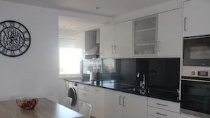 Una cocina moderna con armarios blancos, encimera negra y electrodomésticos de acero inoxidable.