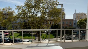 Un balcón con una mesa y sillas blancas, que da a un estacionamiento y edificios.