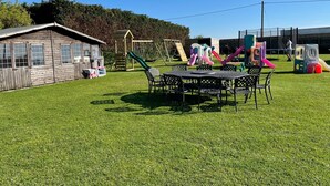 Ein Spielplatz mit Rutschen, Schaukeln und einem hölzernen Spielhäuschen, umgeben von einem Zaun.