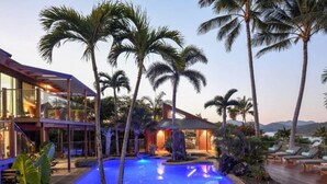 A modern resort with a swimming pool, palm trees, and a deck with lounge chairs.