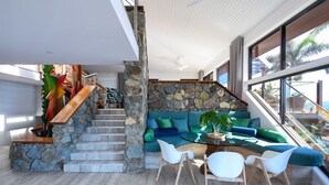 A modern interior with a stone staircase, a blue sofa set, and a glass dining table.