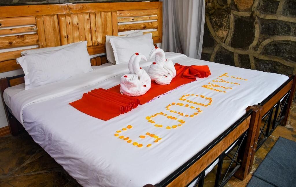 A neatly made bed with white linens, two swan-shaped towels, and a red blanket.