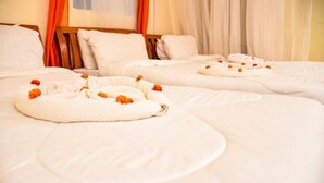 A hotel room with two beds, each with a white bedspread and a towel with orange flowers. - Naivasha Peppercorn Holiday Resort (Naivasha)