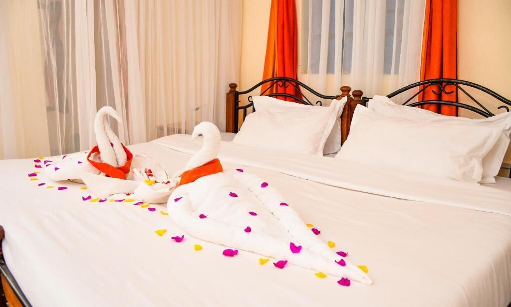 Een hotelkamer met een opgemaakt bed, witte lakens en decoratieve zwanen met oranje details.