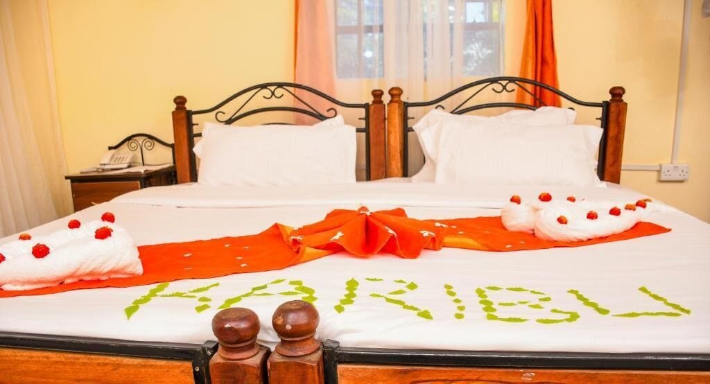 A neatly made bed with a white and orange bedspread, a green embroidered name, and decorative pillows.