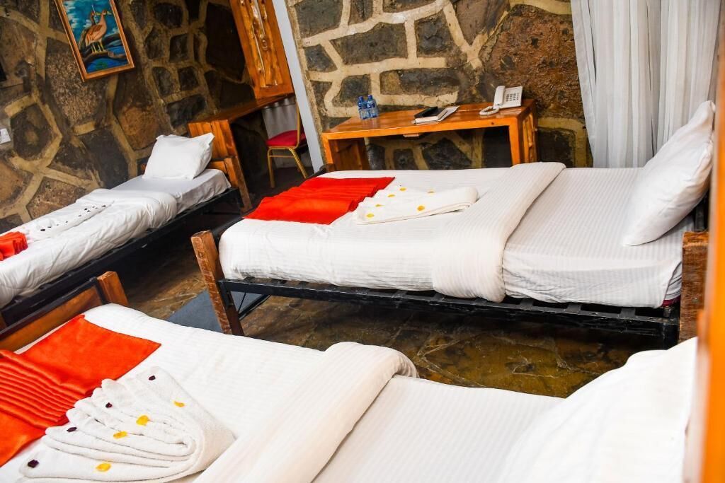 A hotel room with two single beds, a wooden desk, a telephone, and a stone wall.