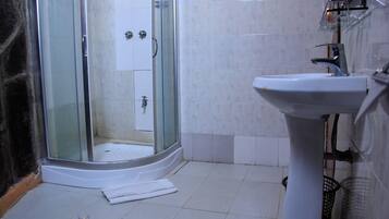 Un baño con cabina de ducha de vidrio, un lavabo blanco y suelo de baldosas.