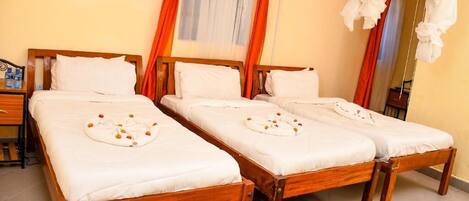 A room with two wooden beds, each with white linens and a towel with orange flowers.