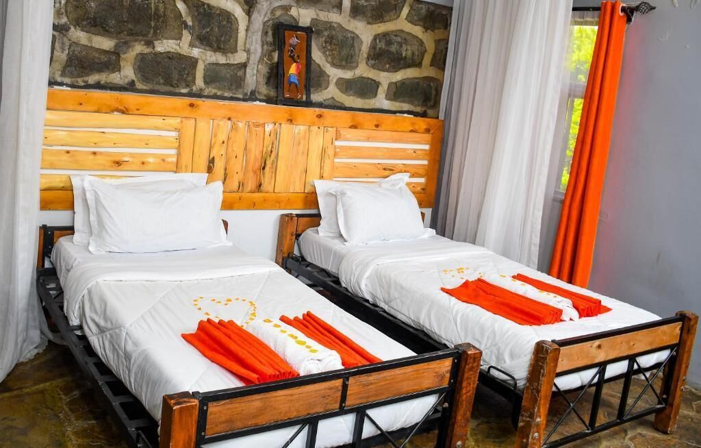 Two single beds with wooden frames and white bedding, a stone wall, and a window with orange curtains.