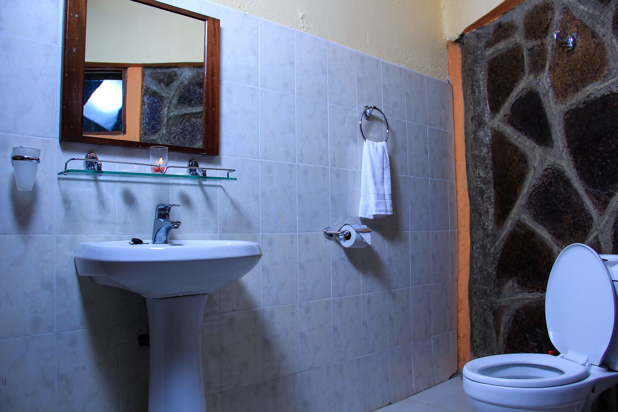 Un baño con lavamanos blanco, espejo, toallero y retrete.