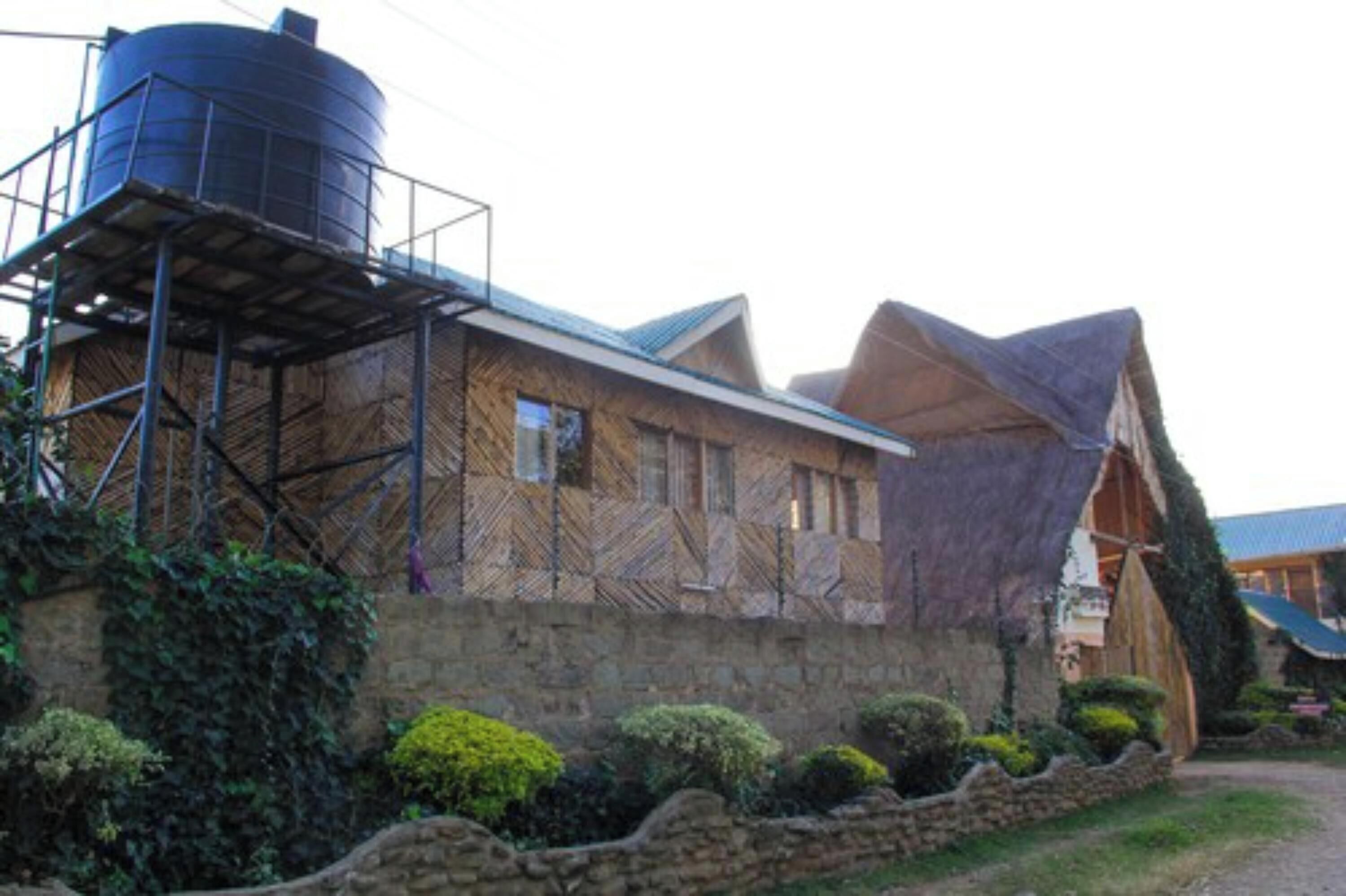 Un edificio rústico con un depósito de agua grande a la izquierda, muros de piedra y techo de paja.