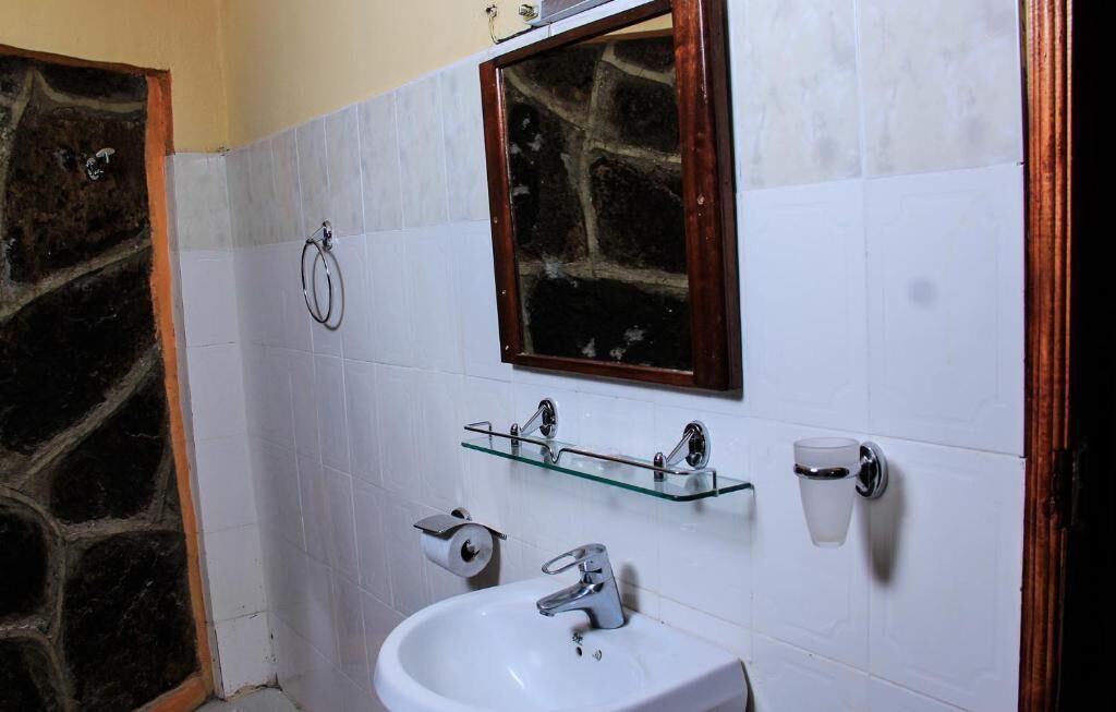 Un baño con pared de piedra, paredes cubiertas de azulejos blancos, un lavamanos con espejo y una repisa de vidrio con artículos de tocador.