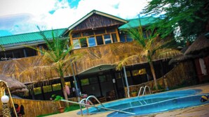 A pool area with a thatched-roof building, palm trees, and a clear sky. - Naivasha Peppercorn Holiday Resort (Naivasha)