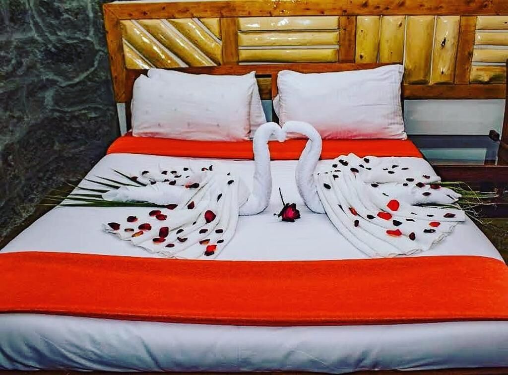 Een bed met een houten hoofdbord, witte beddengoed en een rode deken.